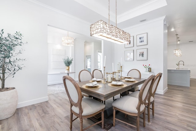 dining area with a chandelier, crown molding, sink, and wood-type flooring