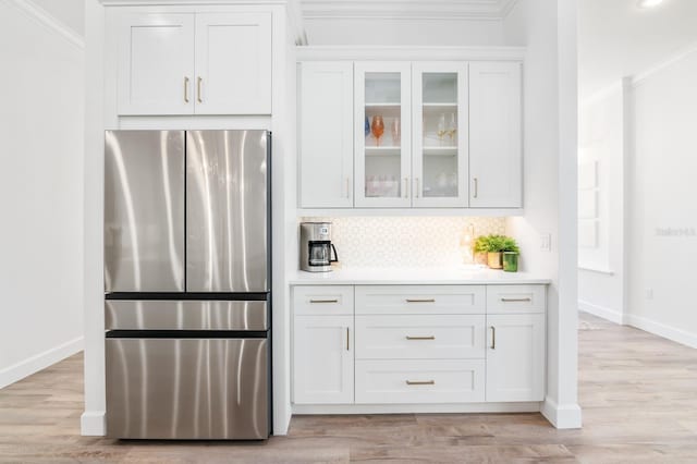 kitchen with stainless steel refrigerator, decorative backsplash, light hardwood / wood-style flooring, and white cabinets