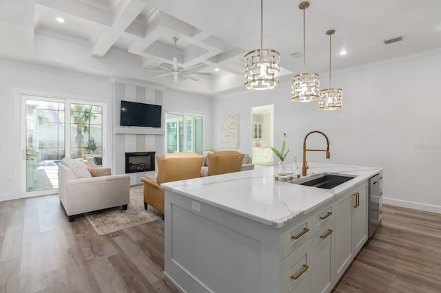 kitchen featuring pendant lighting, a kitchen island with sink, white cabinets, sink, and light stone counters