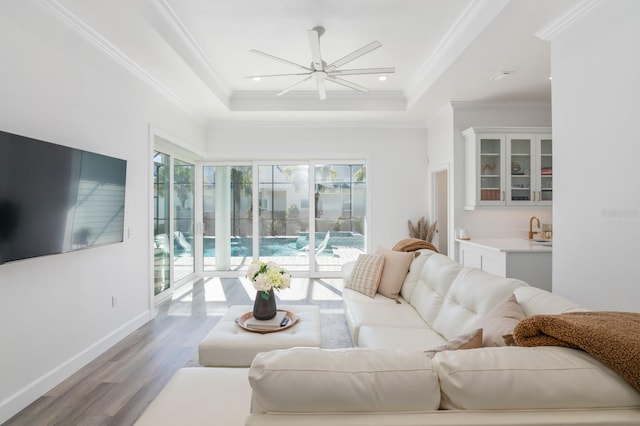 living room with light wood-type flooring, ornamental molding, a tray ceiling, ceiling fan, and sink