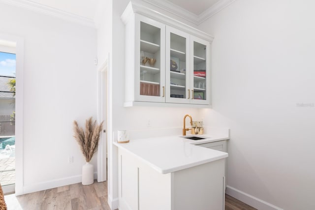 bar with white cabinets, light hardwood / wood-style floors, ornamental molding, and sink