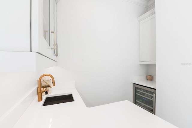 kitchen featuring white cabinets, beverage cooler, ornamental molding, and sink