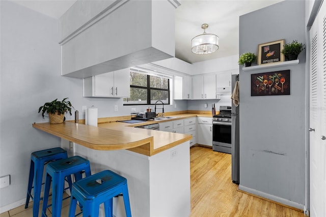 kitchen featuring white cabinets, kitchen peninsula, stainless steel gas range oven, a kitchen bar, and sink