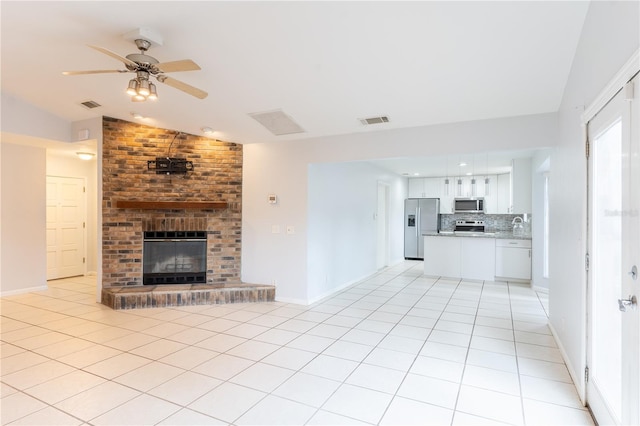 unfurnished living room with a fireplace, lofted ceiling, sink, light tile patterned floors, and ceiling fan