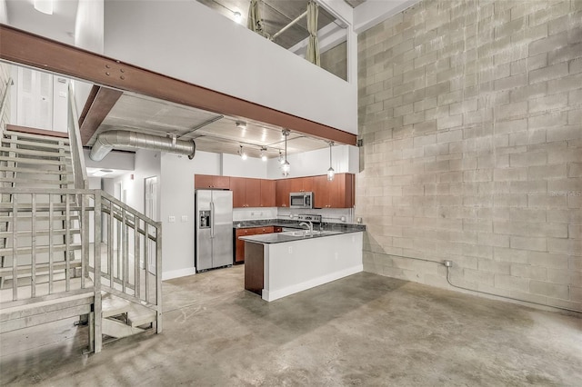 kitchen with concrete flooring, kitchen peninsula, stainless steel appliances, and a high ceiling