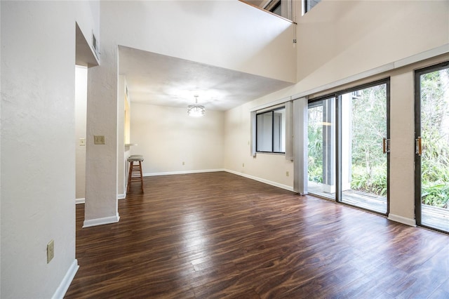 empty room featuring a towering ceiling, a notable chandelier, and dark wood-type flooring