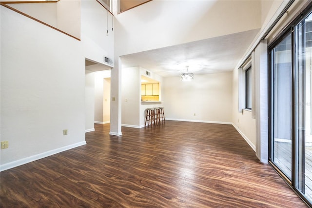 unfurnished living room featuring a high ceiling, a healthy amount of sunlight, a notable chandelier, and dark hardwood / wood-style flooring