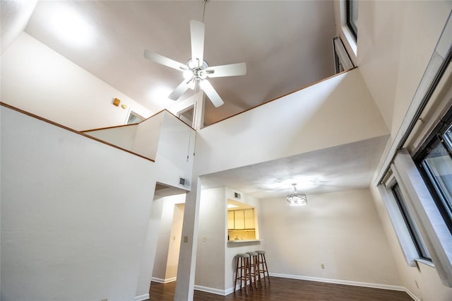 unfurnished living room featuring a high ceiling, dark wood-type flooring, and ceiling fan with notable chandelier