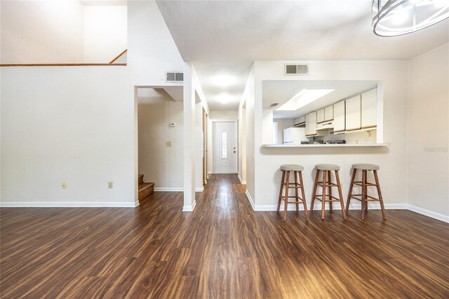 kitchen featuring kitchen peninsula, dark wood-type flooring, white fridge, white cabinetry, and a kitchen breakfast bar