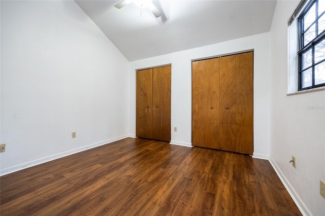 unfurnished bedroom with lofted ceiling, two closets, ceiling fan, and dark hardwood / wood-style flooring