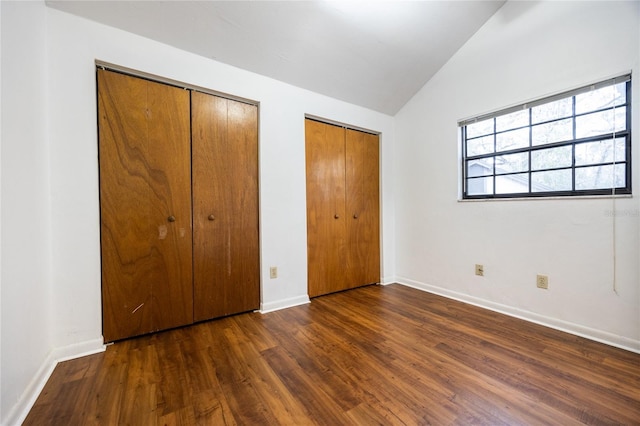 unfurnished bedroom featuring lofted ceiling, dark hardwood / wood-style flooring, and multiple closets