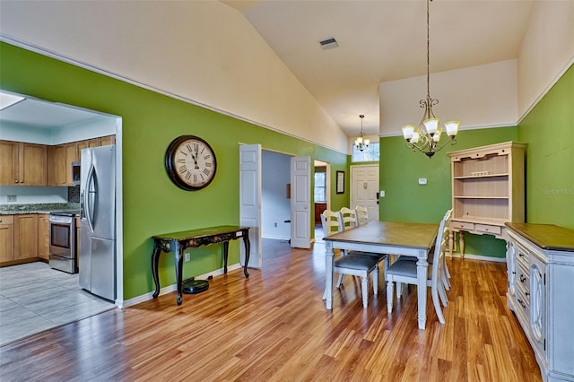 dining area with a notable chandelier, light hardwood / wood-style floors, and high vaulted ceiling