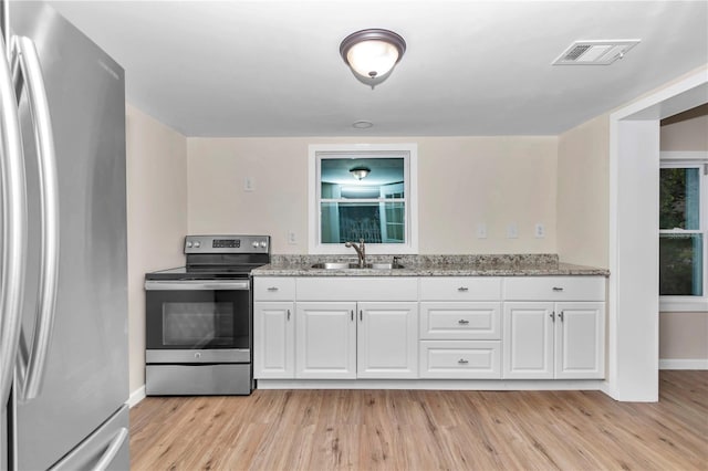 kitchen with white cabinetry, sink, light stone counters, light hardwood / wood-style floors, and appliances with stainless steel finishes