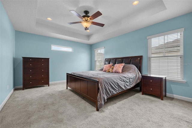 carpeted bedroom with ceiling fan, a tray ceiling, and multiple windows