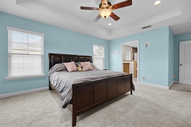 carpeted bedroom with ceiling fan, a tray ceiling, and connected bathroom