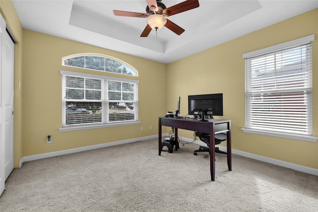 office area featuring a raised ceiling, ceiling fan, and light carpet