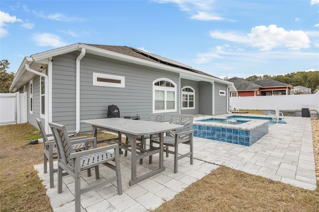 rear view of property with a swimming pool with hot tub, solar panels, and a patio