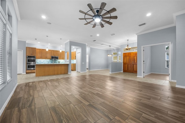 unfurnished living room with ceiling fan with notable chandelier and ornamental molding