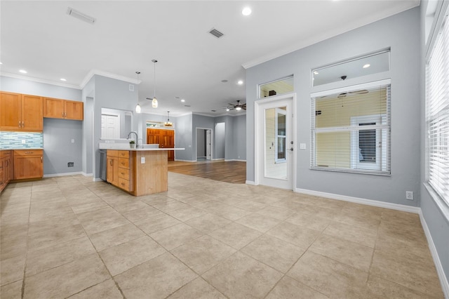 kitchen with decorative light fixtures, ceiling fan, decorative backsplash, a kitchen island with sink, and crown molding