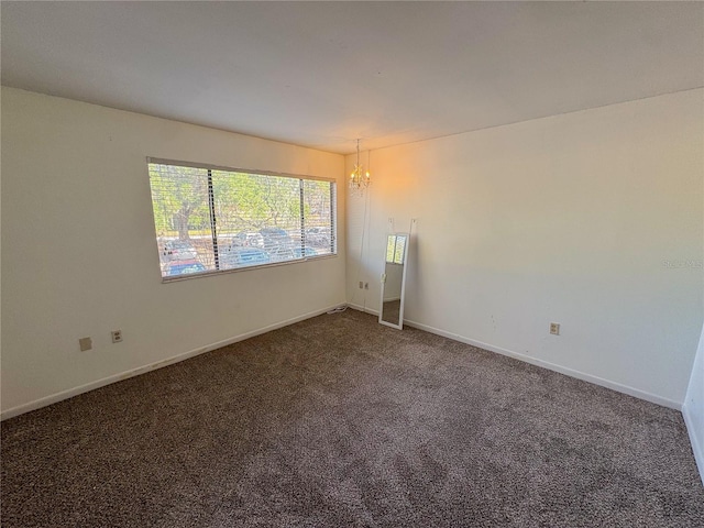 empty room featuring a chandelier and dark colored carpet