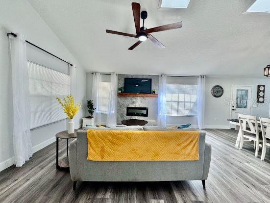 living room with hardwood / wood-style flooring, a textured ceiling, a skylight, a fireplace, and ceiling fan