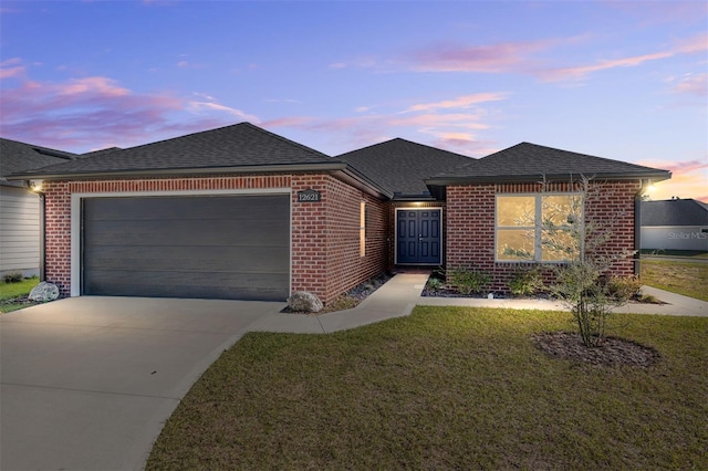 ranch-style house with concrete driveway, brick siding, a lawn, and roof with shingles