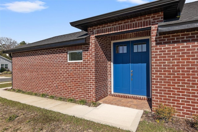 view of exterior entry featuring a shingled roof and brick siding