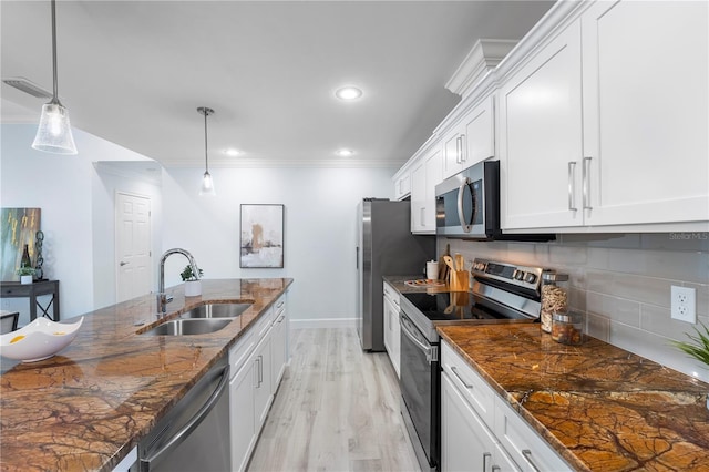 kitchen with white cabinets, appliances with stainless steel finishes, a sink, crown molding, and backsplash