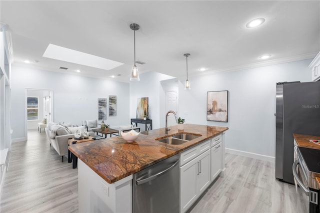 kitchen featuring a skylight, a center island with sink, stainless steel appliances, crown molding, and a sink