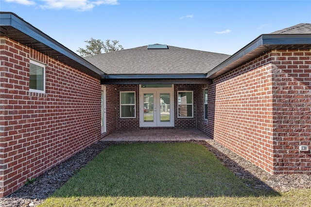 property entrance with french doors, roof with shingles, a yard, a patio, and brick siding