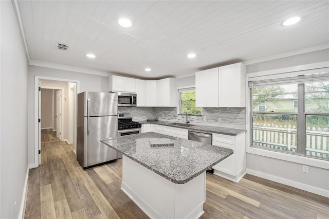 kitchen with light stone countertops, a center island, decorative backsplash, white cabinetry, and appliances with stainless steel finishes