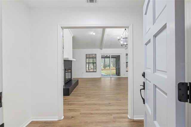 foyer featuring beam ceiling, light hardwood / wood-style flooring, an inviting chandelier, and a tile fireplace