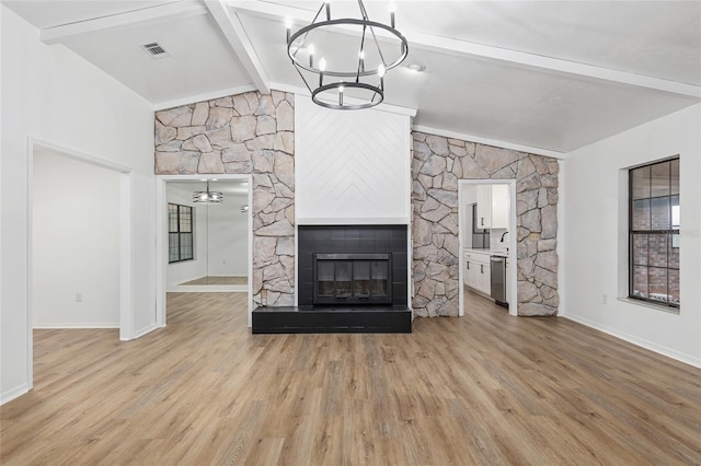 unfurnished living room featuring light wood-type flooring, an inviting chandelier, lofted ceiling with beams, and a fireplace