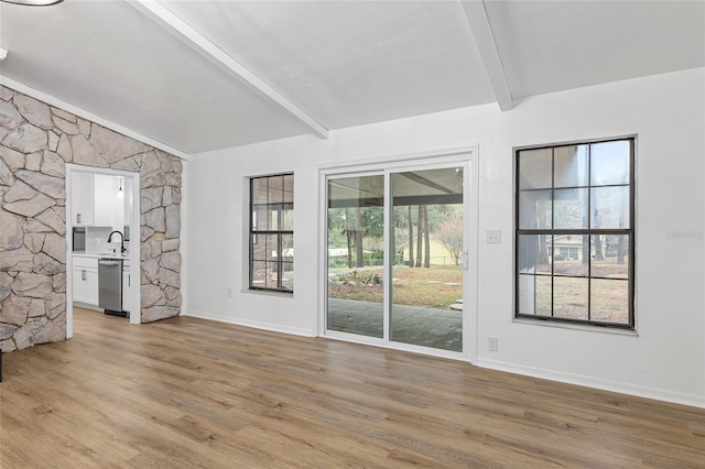 unfurnished living room with beam ceiling, light hardwood / wood-style floors, a healthy amount of sunlight, and sink