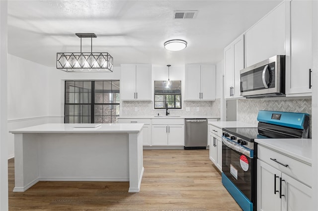 kitchen with appliances with stainless steel finishes, white cabinetry, decorative light fixtures, and sink