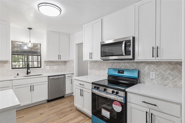 kitchen featuring appliances with stainless steel finishes, light hardwood / wood-style floors, pendant lighting, white cabinets, and sink