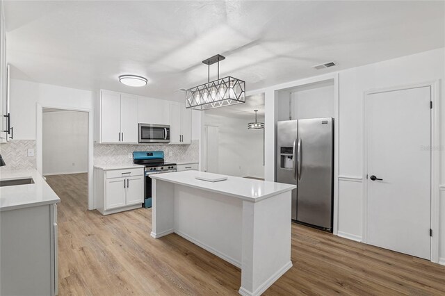 kitchen with stainless steel appliances, white cabinets, light hardwood / wood-style floors, tasteful backsplash, and hanging light fixtures