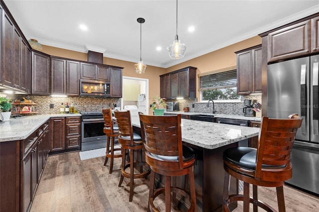 kitchen with hardwood / wood-style floors, appliances with stainless steel finishes, hanging light fixtures, a kitchen island, and dark brown cabinetry