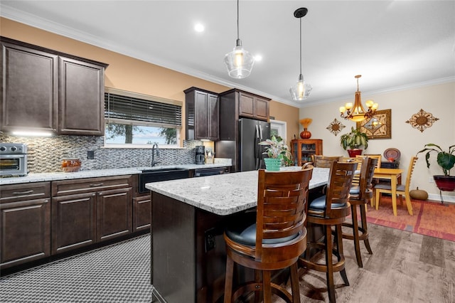 kitchen with ornamental molding, dark brown cabinetry, a kitchen island, pendant lighting, and stainless steel fridge