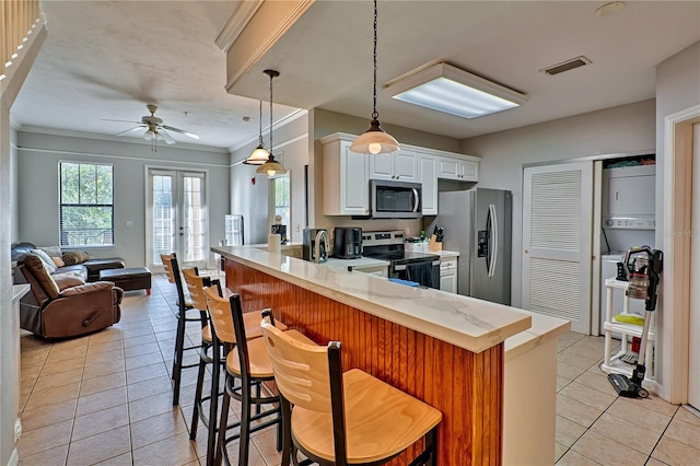 kitchen featuring kitchen peninsula, light tile patterned floors, a kitchen bar, white cabinets, and appliances with stainless steel finishes