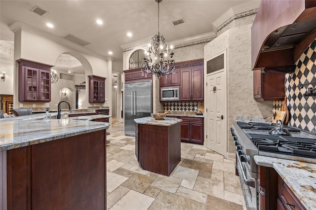 kitchen featuring built in appliances, premium range hood, a kitchen island, pendant lighting, and a notable chandelier