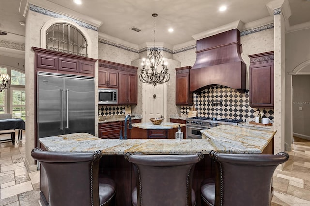 kitchen featuring built in appliances, decorative light fixtures, ornamental molding, premium range hood, and a kitchen island