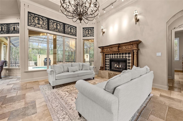 living room with a notable chandelier, crown molding, a tile fireplace, and a towering ceiling