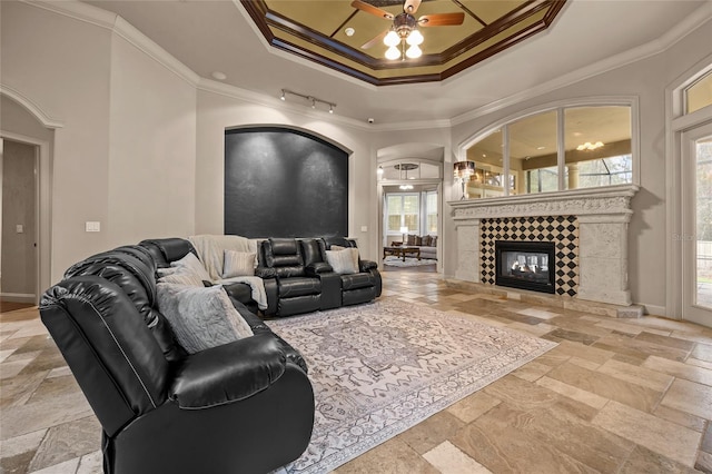 living room with a tiled fireplace, ceiling fan, rail lighting, a tray ceiling, and crown molding