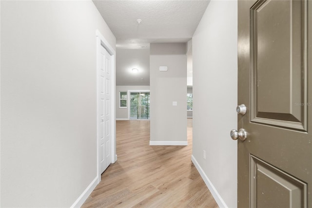 corridor with a textured ceiling and light hardwood / wood-style flooring