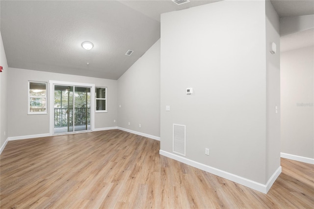 spare room featuring a textured ceiling, vaulted ceiling, and light hardwood / wood-style floors