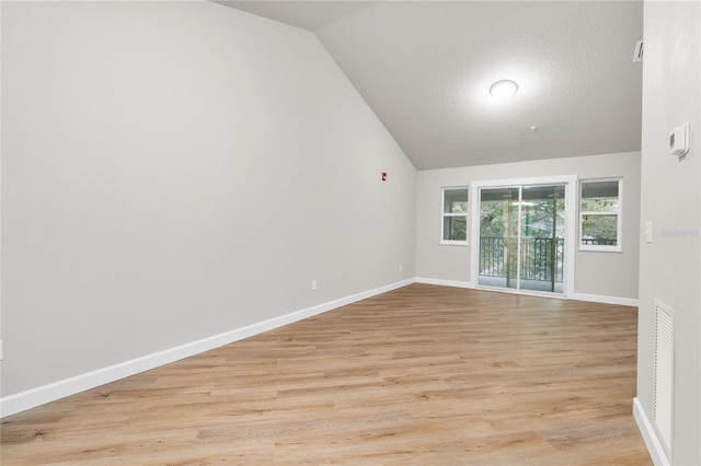 empty room featuring a textured ceiling, light wood-type flooring, and lofted ceiling