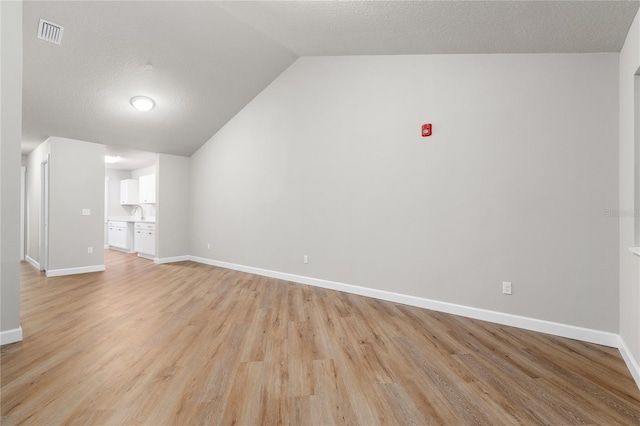 unfurnished living room featuring lofted ceiling, a textured ceiling, and light hardwood / wood-style floors