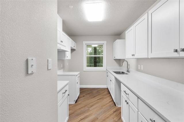 kitchen with sink, white cabinets, a textured ceiling, dishwasher, and light hardwood / wood-style flooring