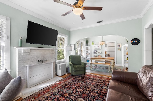 living room featuring ceiling fan, ornamental molding, and a brick fireplace